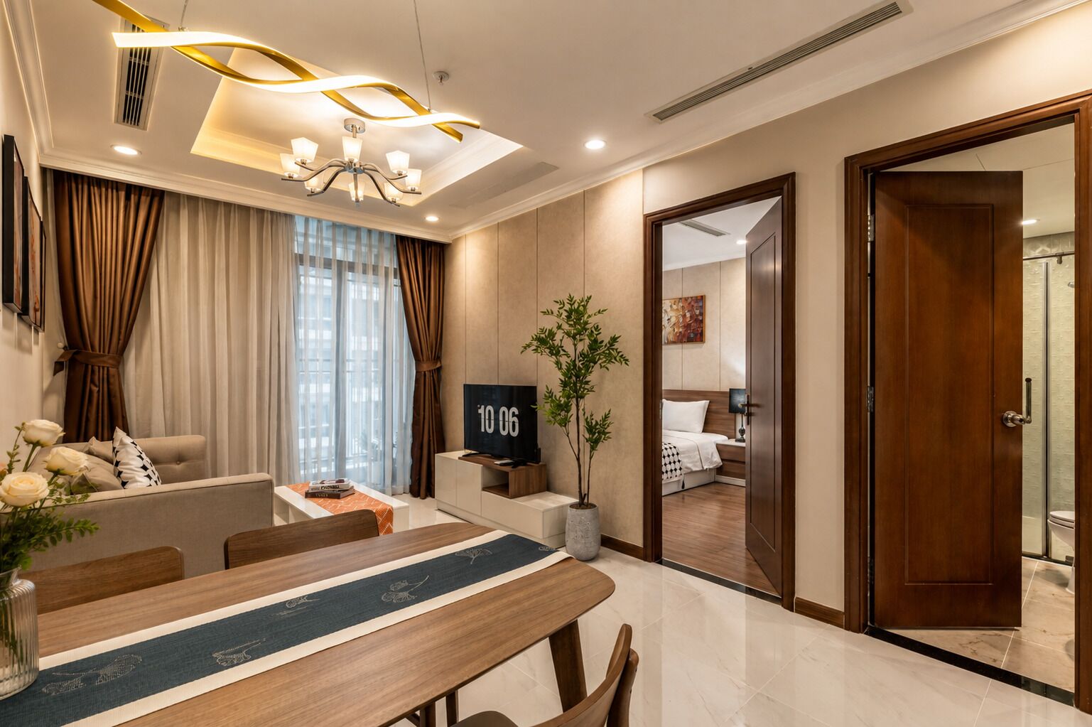 A modern hotel room with a dining area, a TV, a potted plant, and a visible bathroom.