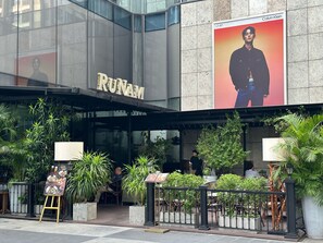 En restaurant kaldet RUNAM med udendørs siddepladser og et stort Calvin Klein-plakat på bygningen.