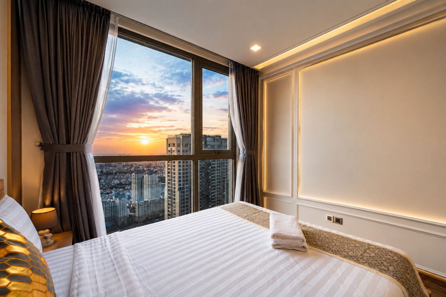A hotel room with a large bed, a view of the cityscape, and a window with curtains.