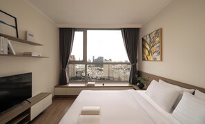 A hotel room with a large bed, a TV, a bookshelf, and a window with a city view. - Vinhomes Central Park Premier Apartment (Ho Chi Minh City)