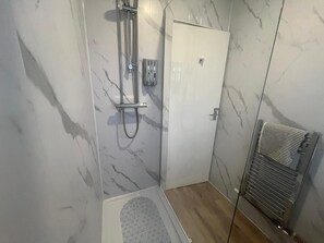Bathroom features a glass-enclosed shower area with handheld showerhead and control panel.