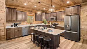 A modern kitchen with wooden paneling, stainless steel appliances, and a central island with stools. - Mountain Views ~5-King BD~Gameroom~HotTub~Firepit (Sevierville)