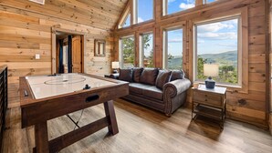 A wooden interior with a pool table, a sofa, and large windows offering a view of the outdoors. - Mountain Views ~5-King BD~Gameroom~HotTub~Firepit (Sevierville)