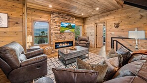 A cozy cabin interior with a stone fireplace, leather sofas, and a wooden ceiling. - Mountain Views ~5-King BD~Gameroom~HotTub~Firepit (Sevierville)