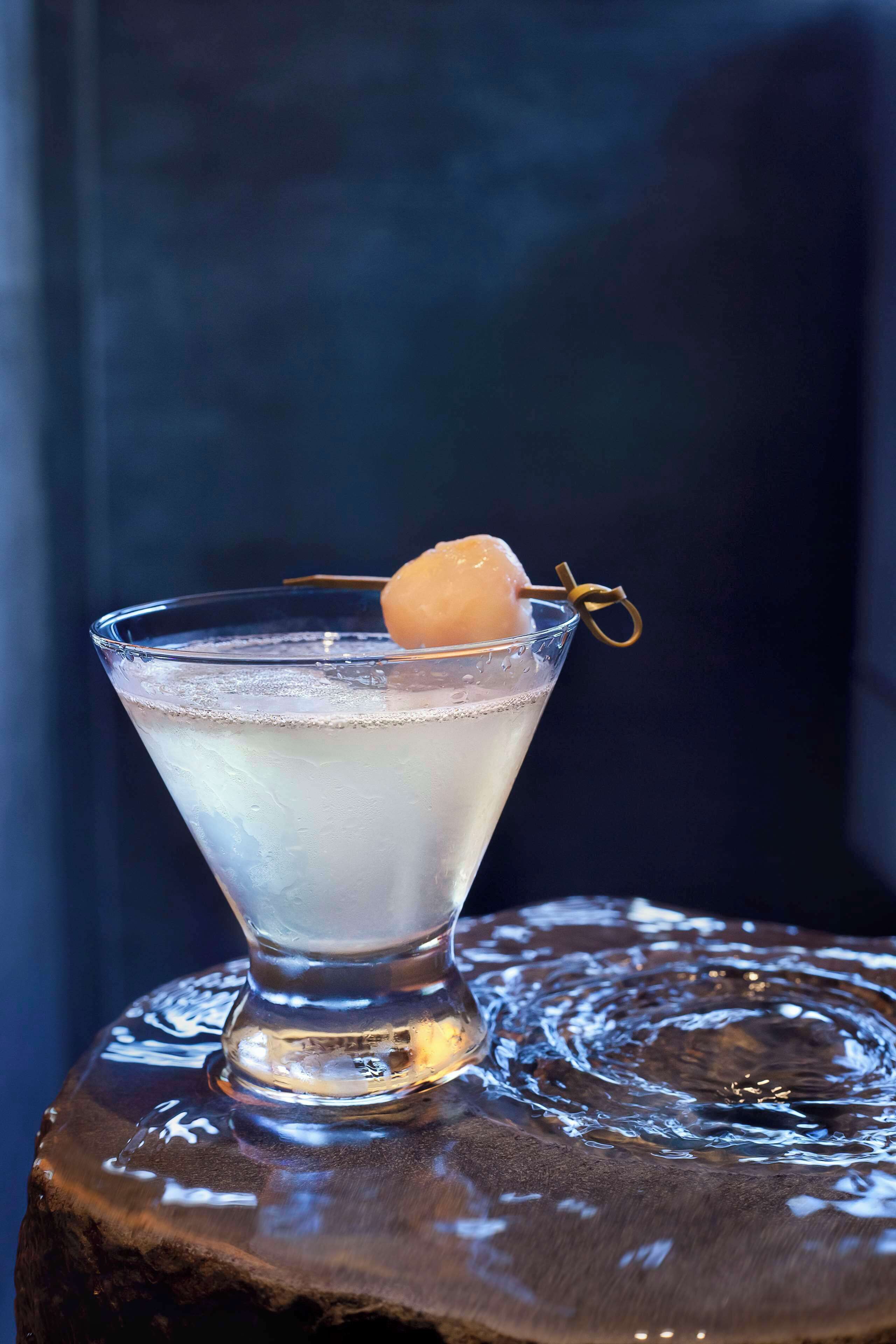 Un got de martini amb un líquid transparent i una taronja com a guarnició sobre una superfície de fusta.