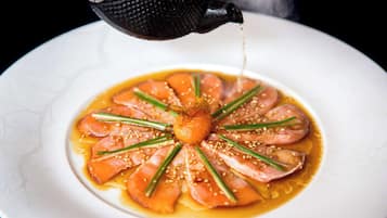 A plate of food with a central garnish, surrounded by slices of salmon and garnished with sesame seeds and green herbs.