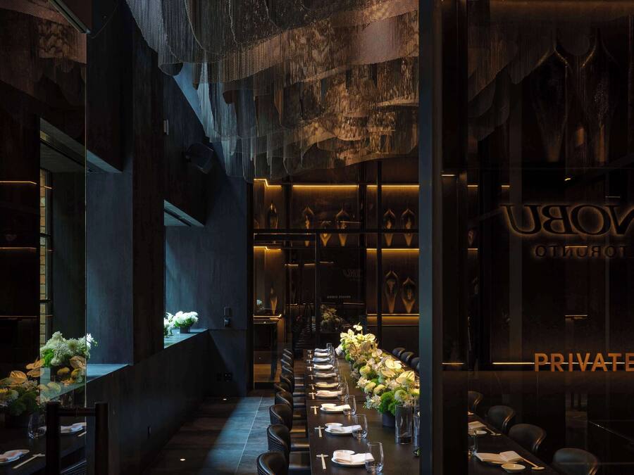 A private dining area with a long table set for a meal, flanked by dark walls and decorative lighting.