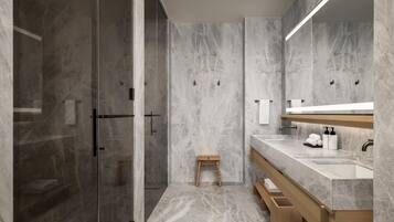 A modern bathroom with a glass shower enclosure, a wooden stool, a marble vanity, and a large mirror.