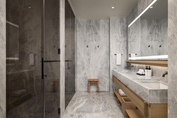 Une salle de bain moderne avec une douche à parois de verre, un tabouret en bois, un meuble-lavabo en marbre et un grand miroir.