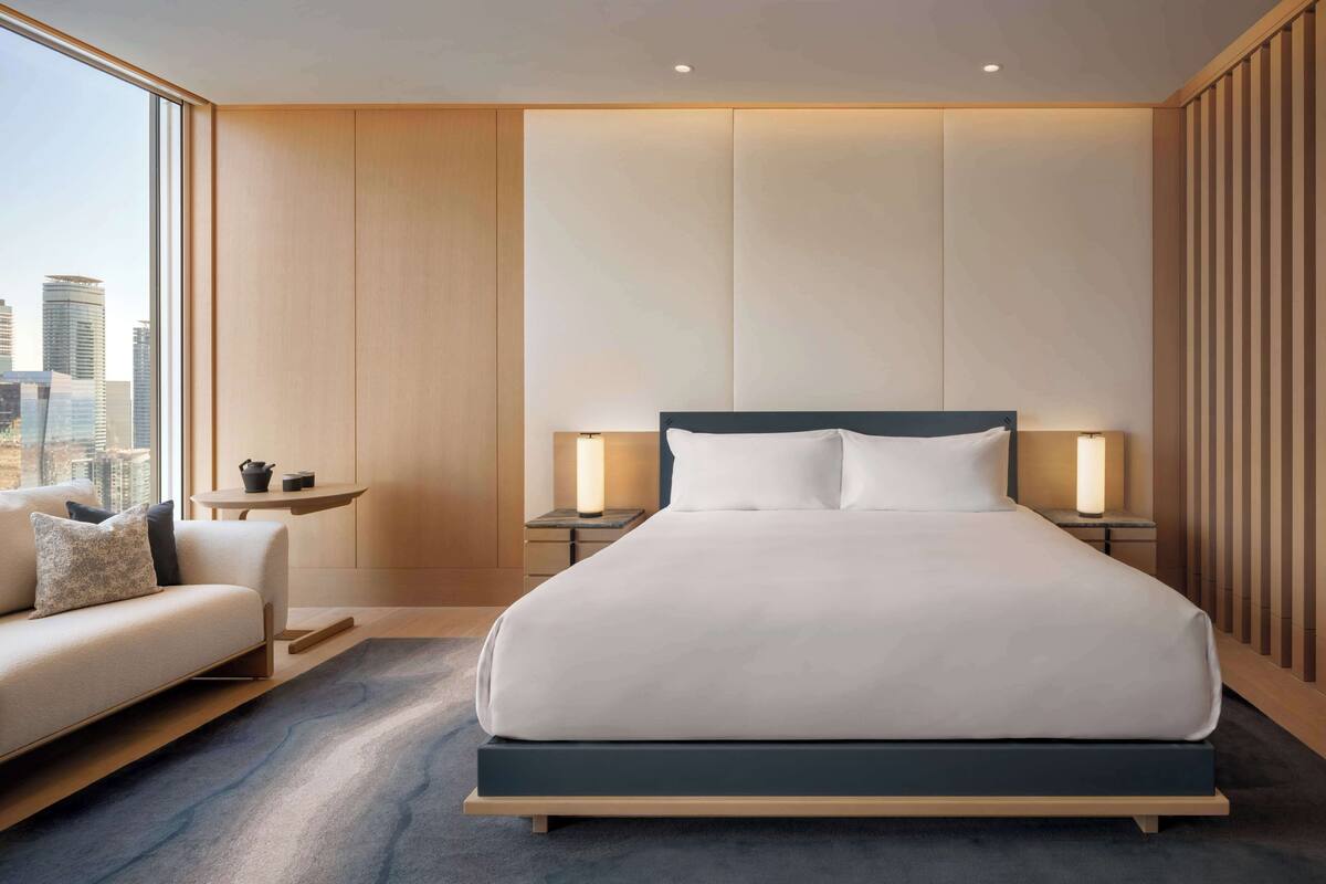 Et moderne hotelværelse med en stor seng, sengeborde, en sofa og udsigt over byen.