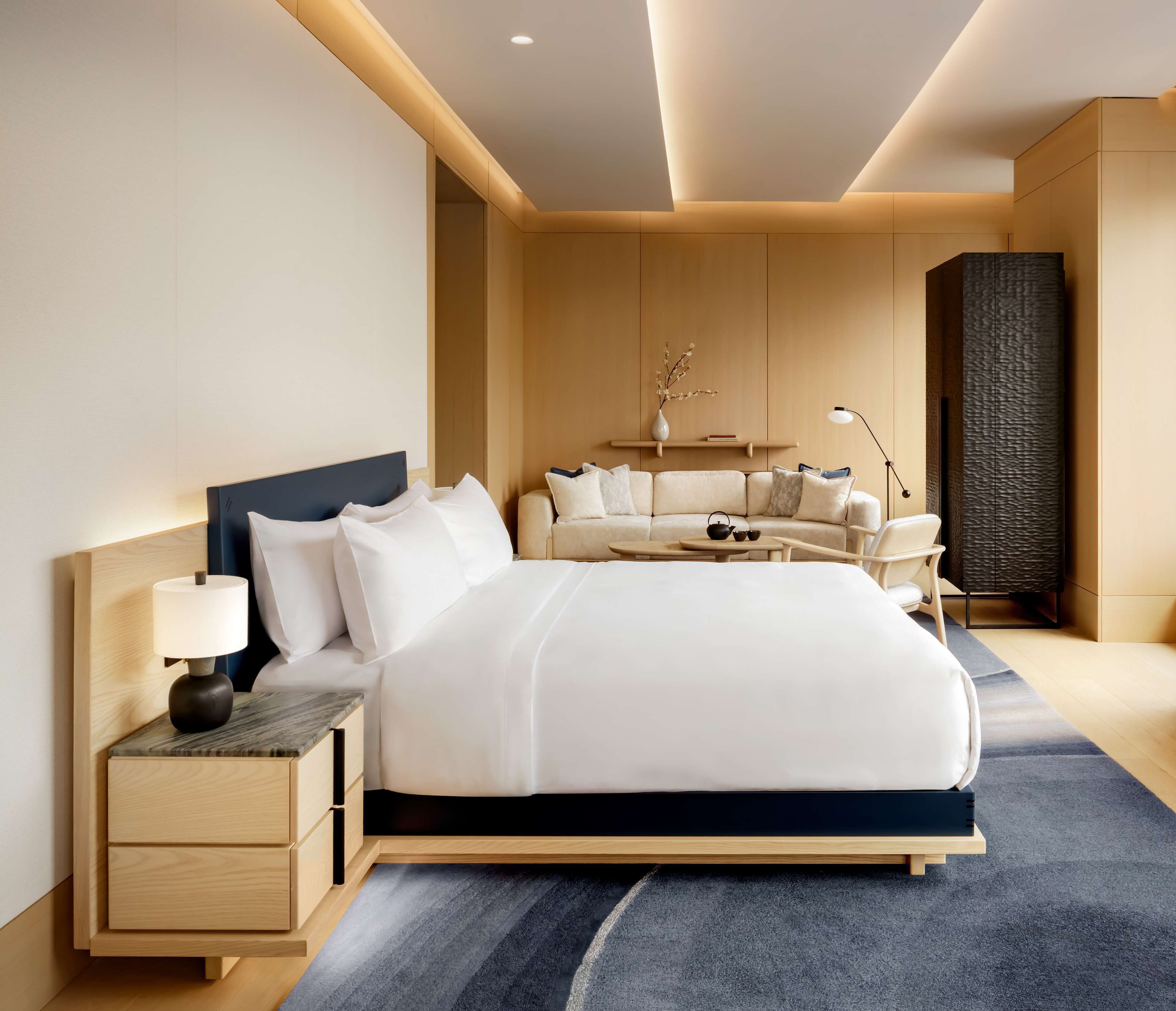A modern hotel room with a large bed, bedside tables, a sofa, and a decorative wall panel.