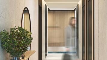 A modern hallway with a minimalist design, featuring a potted plant on a wooden shelf, a large mirror, and a person walking towards a wooden door.