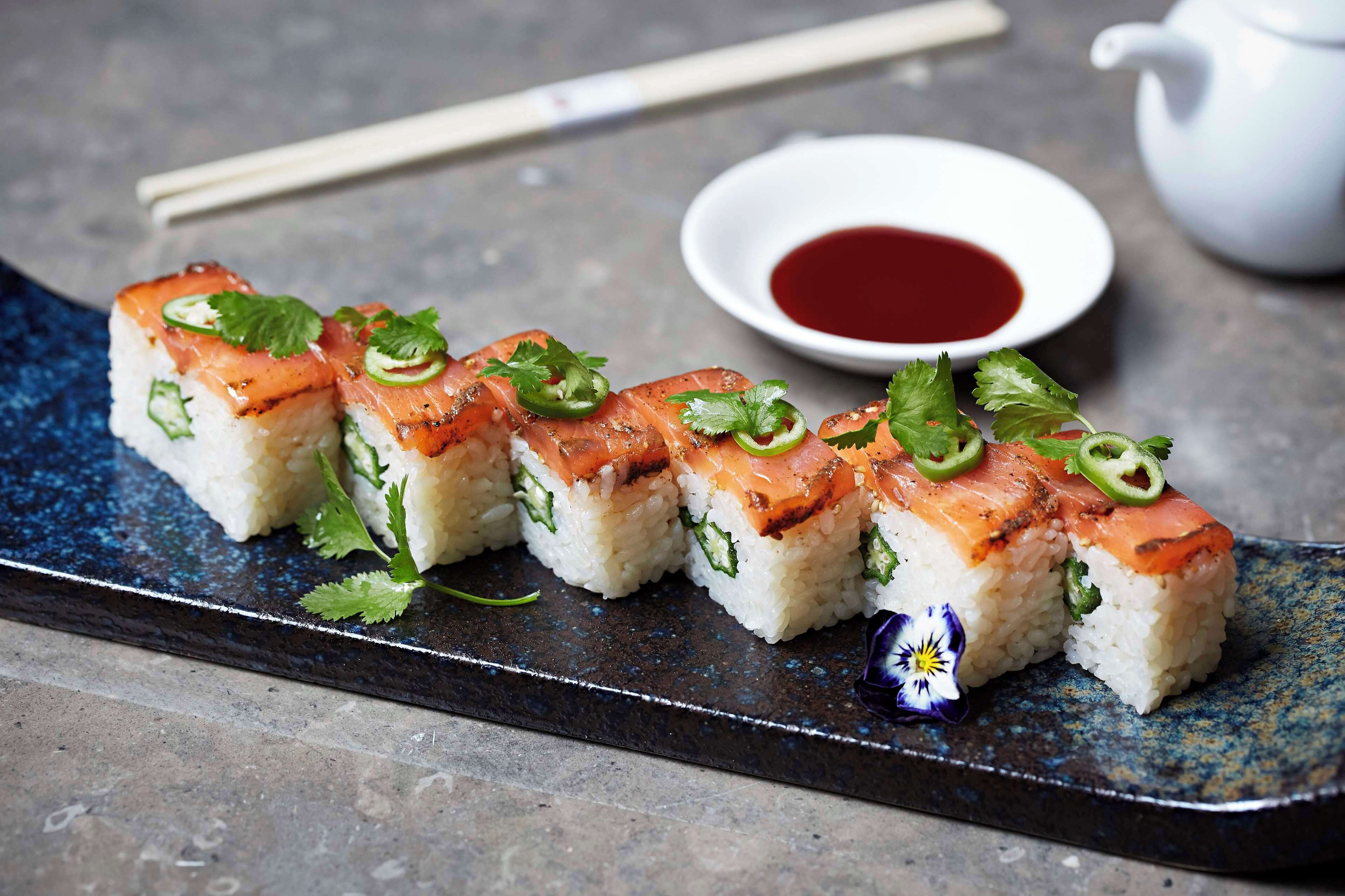 Sushi rolls with a side of soy sauce on a dark plate.