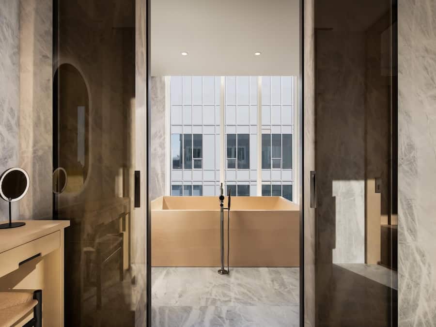 Un baño moderno con una bañera, un espejo redondo y suelo de mármol.