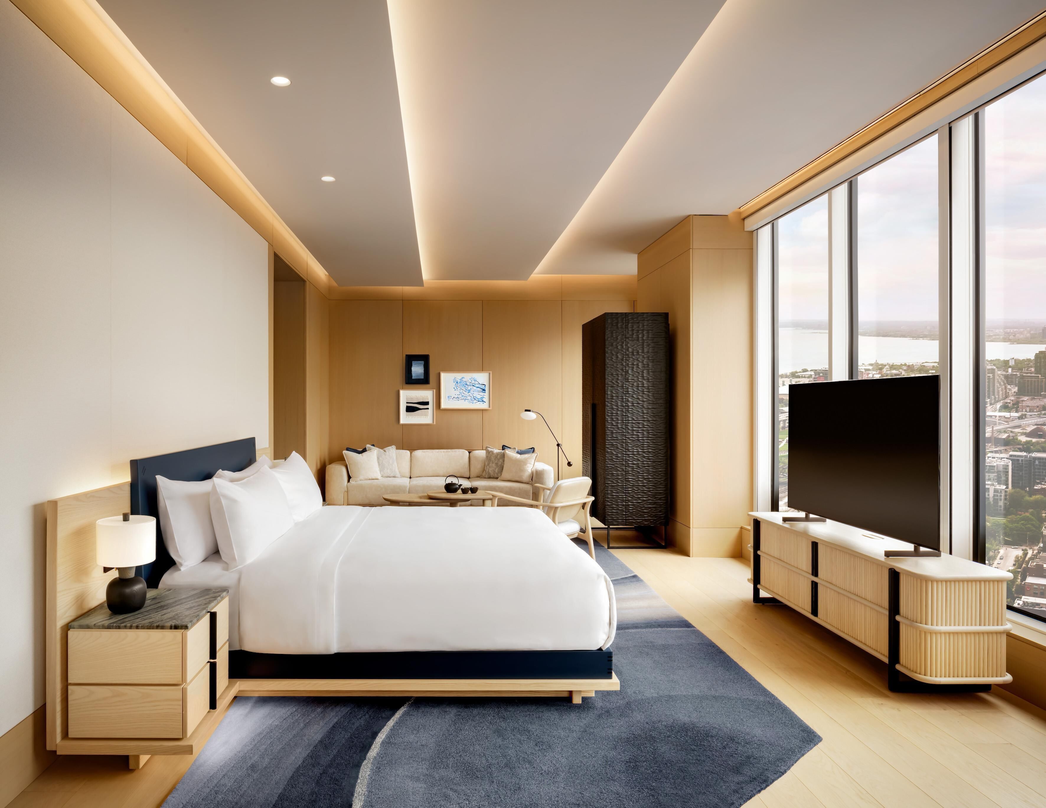 A modern hotel room with a large bed, a flat-screen TV, a sofa, and a city view.
