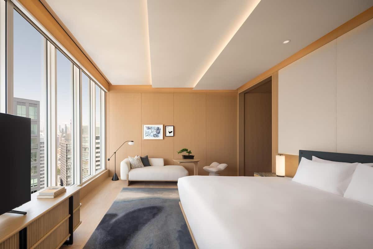 Et moderne hotelværelse med en stor seng, en sofa, et skrivebord med et fjernsyn og udsigt over byen.