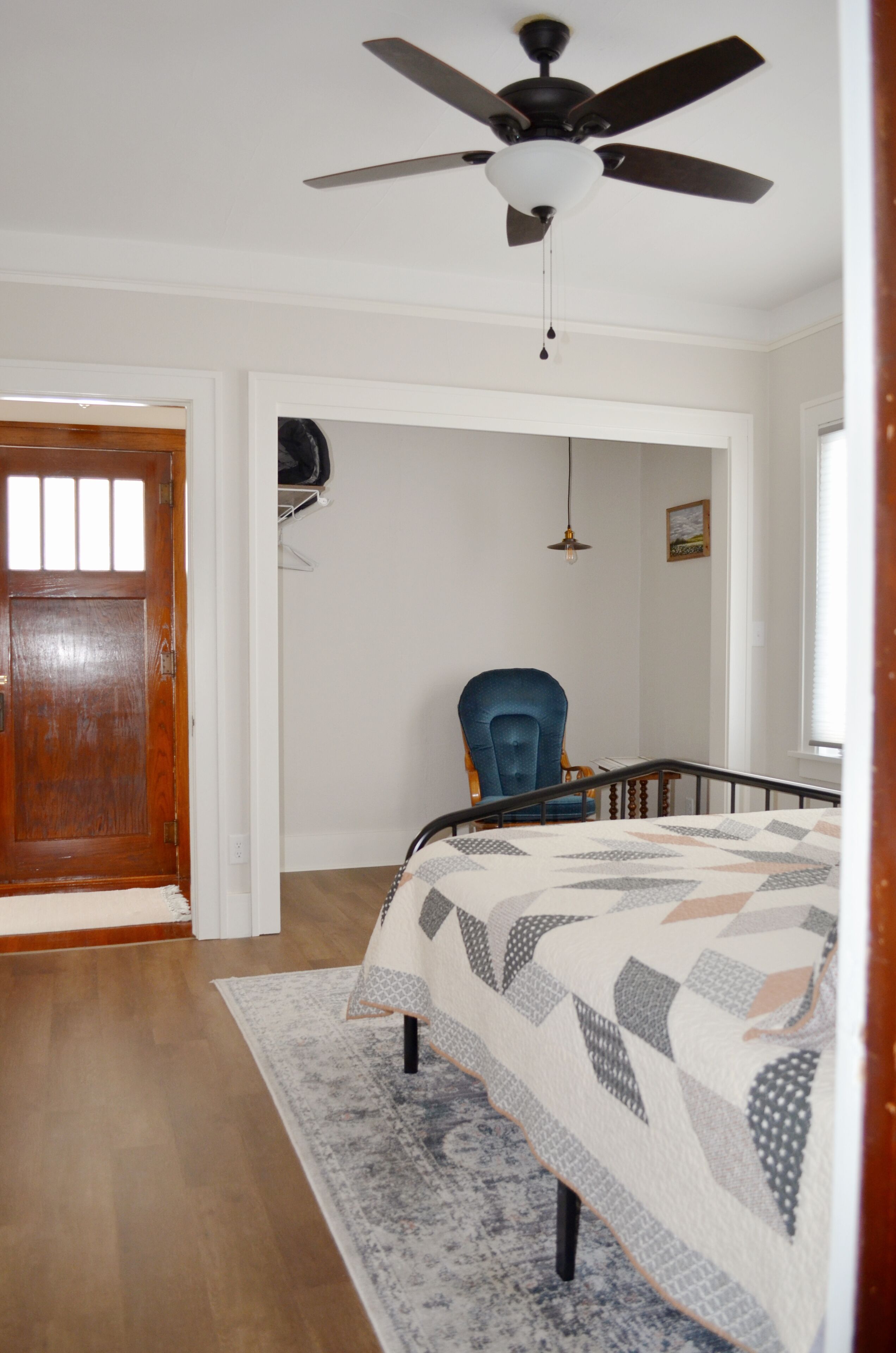 A bedroom with a bed, a ceiling fan, a wooden door, and a chair.