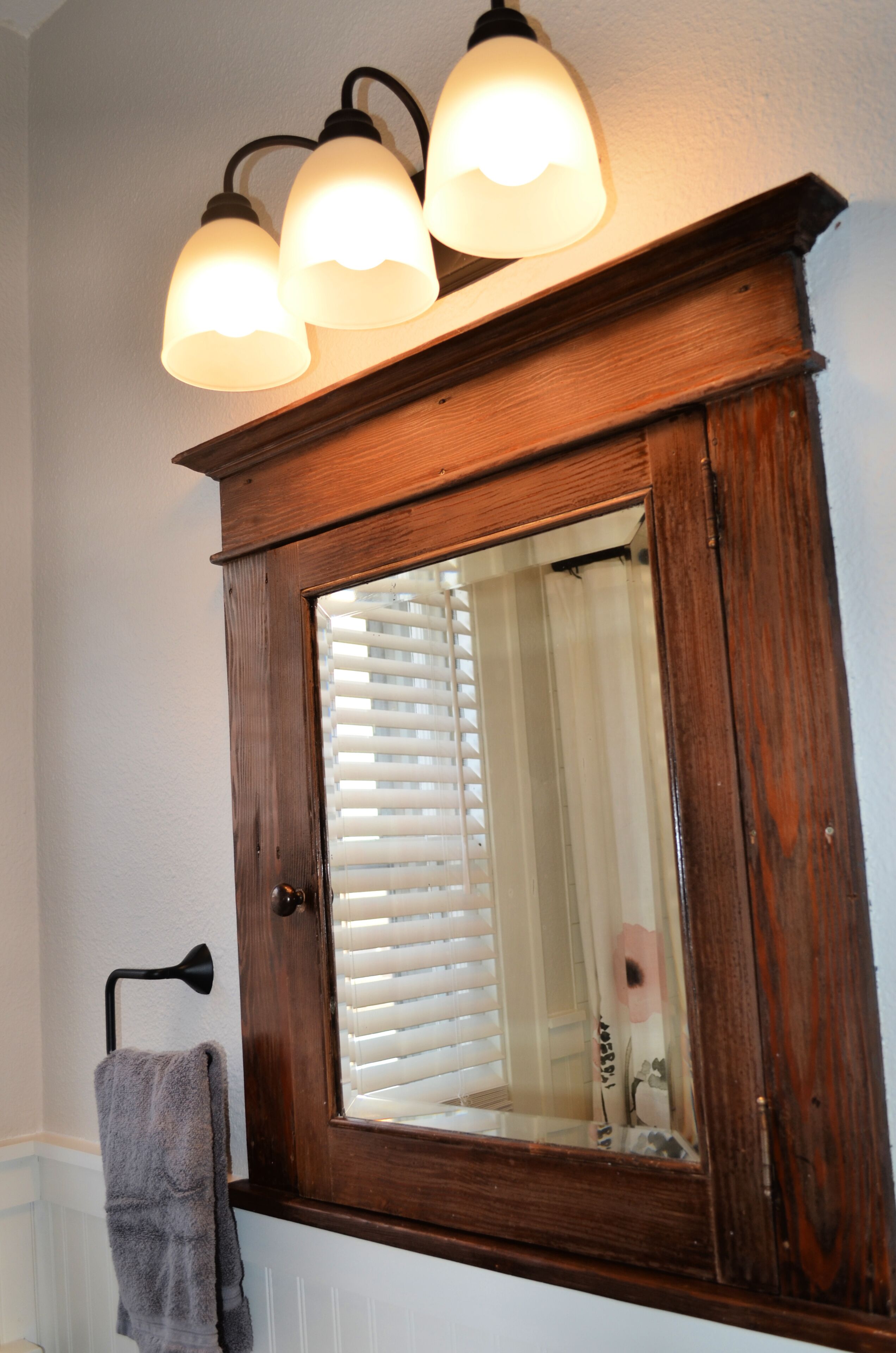 A wooden medicine cabinet with a mirror, a towel rack, and a light fixture above it.