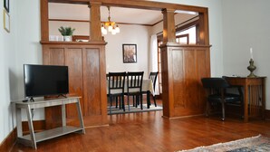 A living room with a wooden floor, a TV on a stand, a dining table with chairs, and a patterned rug. - Wild Rose Cottage



Save
 (De Smet)