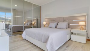 A modern bedroom with a large bed, bedside tables with lamps, and a sliding glass door leading to a balcony. - Villa Quinta Grande (Camara de Lobos)