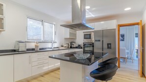 A modern kitchen with white cabinets, a central island, a stainless steel range hood, and a microwave. - Villa Quinta Grande (Camara de Lobos)