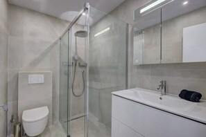 A modern bathroom with a glass-enclosed shower, a white toilet, and a white vanity with a sink.
