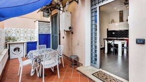 Eine Terrasse im Freien mit Tisch und Stühlen, einer Waschmaschine und einem blauen Sonnensegel.