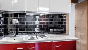 Eine moderne Küche mit weißer Arbeitsplatte, schwarzer Fliesenrückwand und roten Schränken.