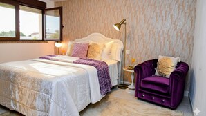 Een slaapkamer met een bed, nachtkastje, lamp en een paarse fauteuil.