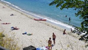 Een strand met mensen die zonnebaden en zwemmen, een boot op het water, en een bebost heuvel in de verte.