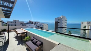 A rooftop pool with a view of the sea, surrounded by modern buildings.