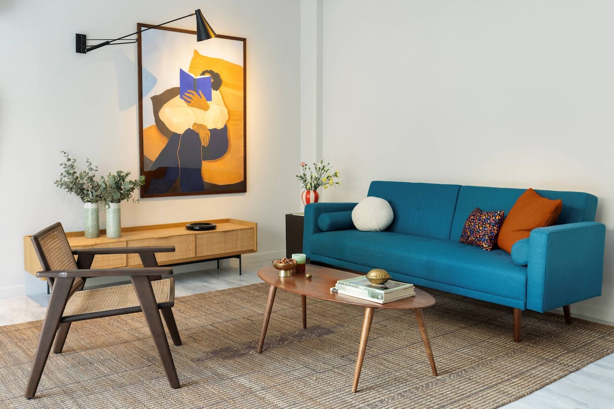 Una sala moderna con un sofá azul, una mesa de centro de madera, una silla, una mesita auxiliar y un cuadro abstracto grande en la pared.