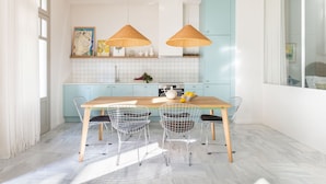 A modern kitchen with a wooden table, wire chairs, and two hanging light fixtures. - Silk n Cotton (Athens)