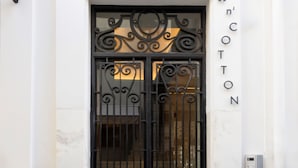 A black wrought iron gate with intricate designs, a white marble wall, and the words "Silk'n'Cotton" on the right. - Silk n Cotton (Athens)