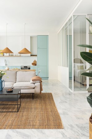 A modern living room with a sofa, coffee table, and a large window. - Silk n Cotton (Athens)