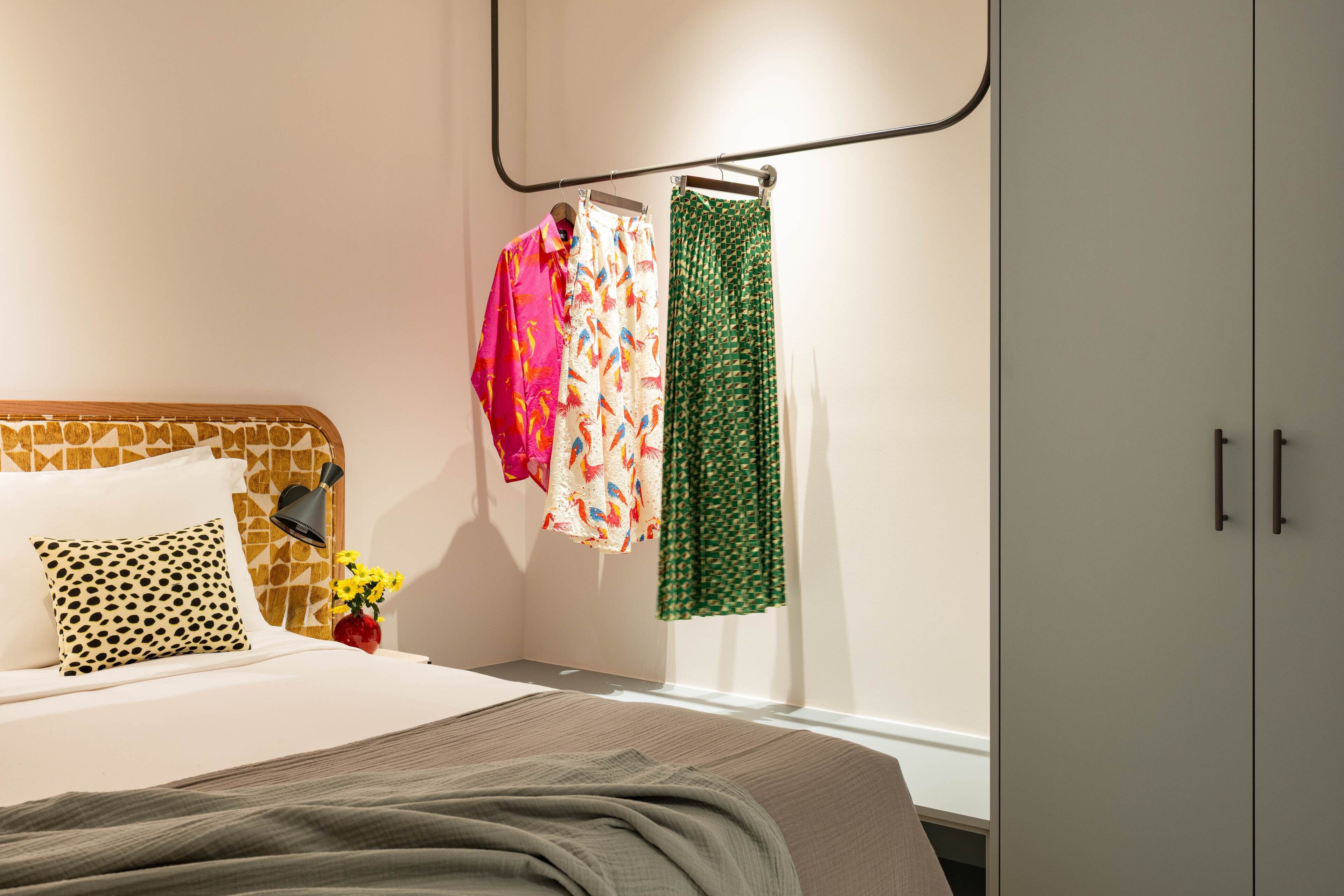 A neatly made bed with a patterned headboard, a bedside lamp, and a vase with flowers.