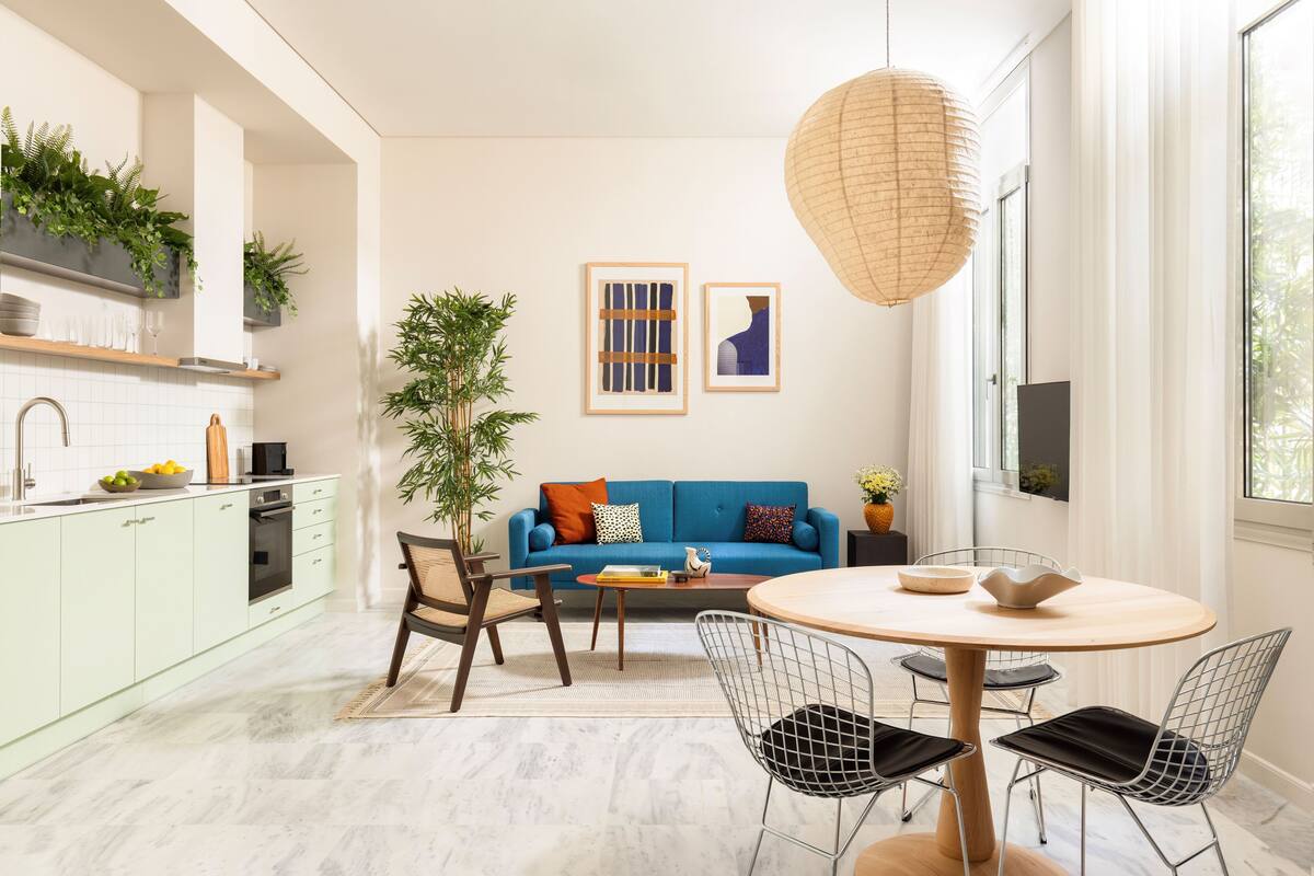 Una cocina moderna con armarios verde claro, un sofá azul y una zona de comedor con sillas de alambre y una mesa redonda.