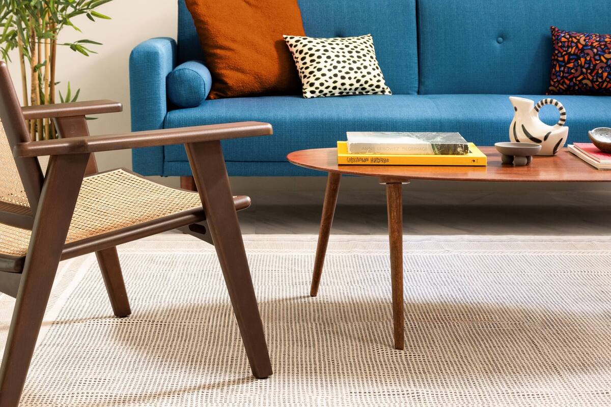 Un salón con un sofá azul, una silla de madera, una mesita con libros y dos cuadros abstractos enmarcados en la pared.