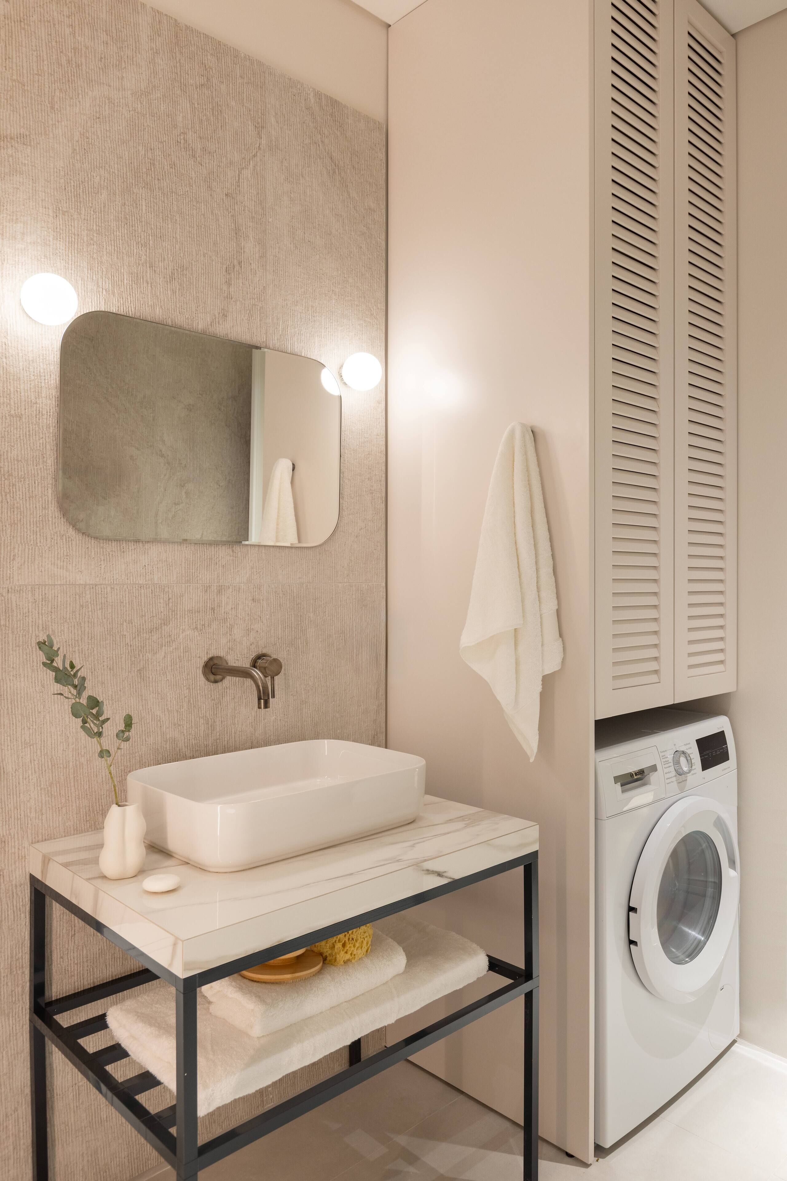 Un baño moderno con lavabo blanco, espejo y lavadora integrada.