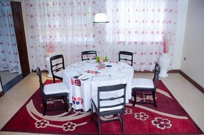 Een eethoek met een ronde tafel, vier stoelen, een vaas met bloemen en een rood vloerkleed met bloemenmotief.