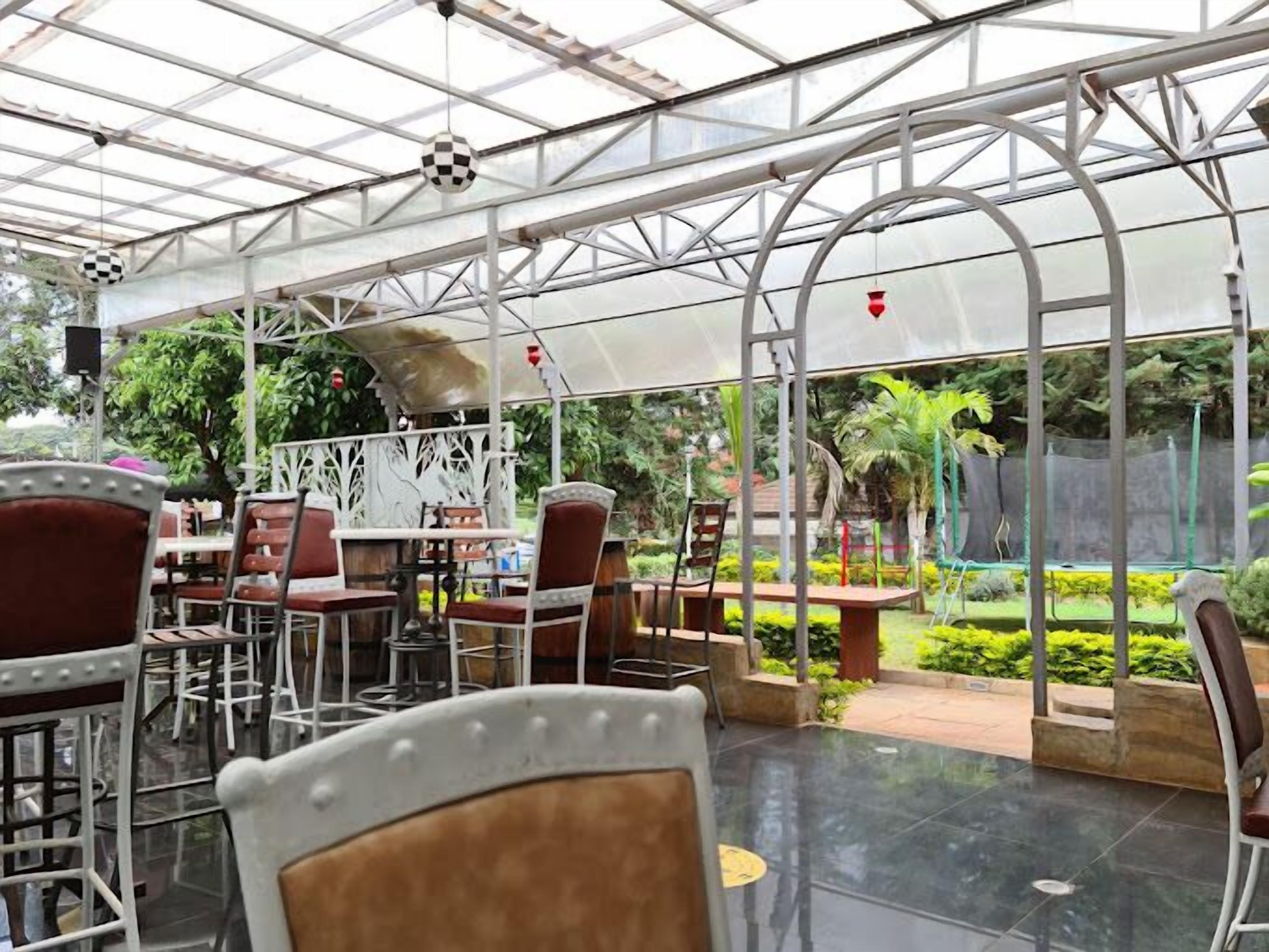 A greenhouse-style restaurant with tables and chairs, large glass windows, and a view of greenery outside.