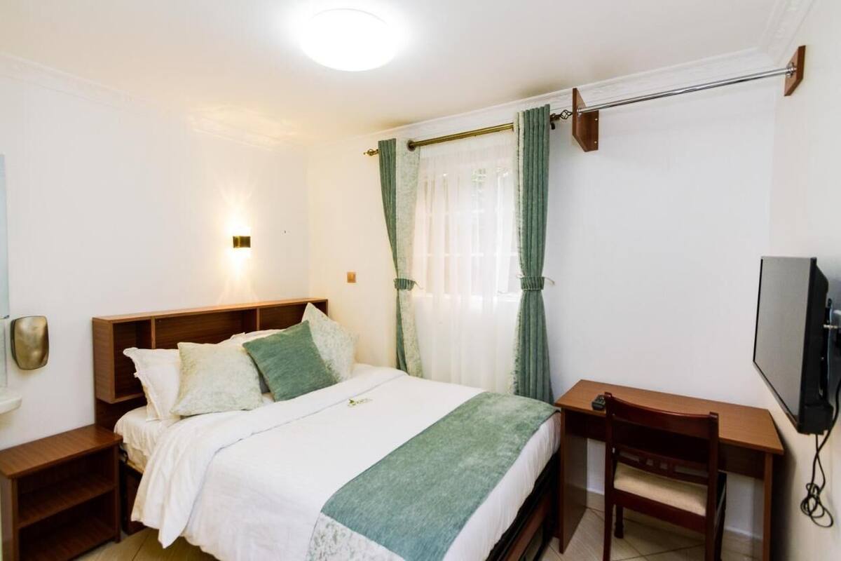 A bedroom with a bed, bedside table, TV, and curtains.