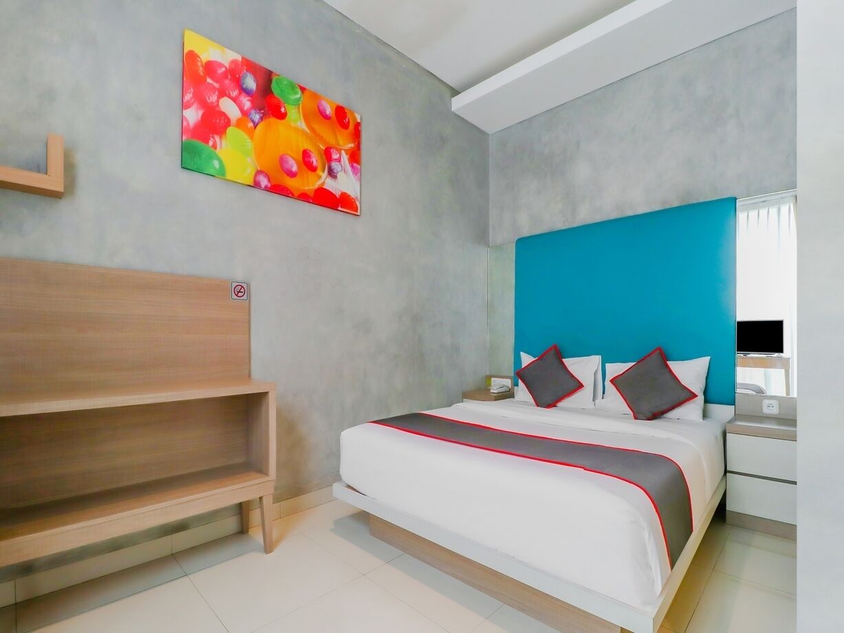 Une chambre d’hôtel moderne avec un lit, un banc en bois, une peinture abstraite aux couleurs vives et un mur d’accent bleu.