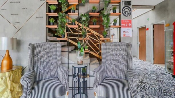 A modern lobby with two checkered armchairs, a central staircase with greenery, and a 'Think' sign on the wall. - The Batik Bed and Coffee (Bandung)