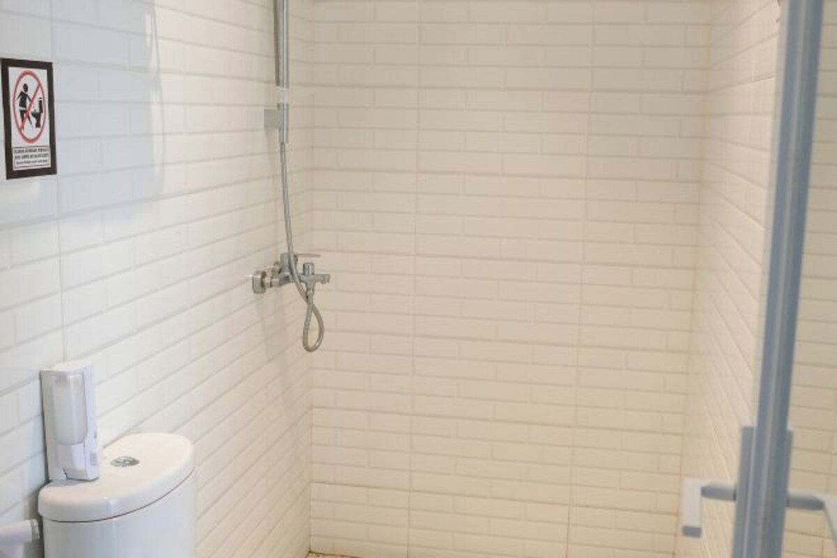 A small, enclosed shower area with white tiled walls and a toilet.