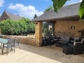 An outdoor patio with stone walls, a covered seating area, and a table with chairs.