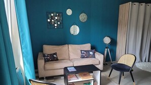 Un salon avec un canapé beige, deux fauteuils, une table basse et une bibliothèque.