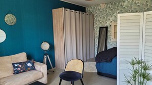 Un salon comprenant un canapé, un fauteuil, une table basse, une lampe, un rideau, une porte et une plante.