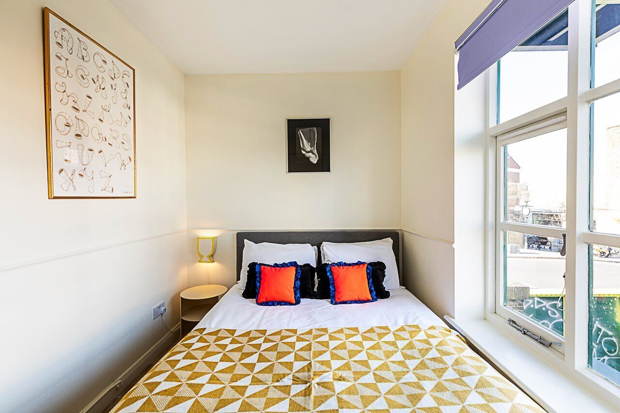 A hotel room with a bed, a framed alphabet art piece, a framed picture on the wall, and a window with a view of the street.