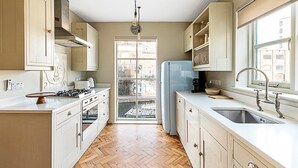 Une cuisine avec des meubles de rangement en bois, une cuisinière à gaz, un évier et une fenêtre donnant sur une cour.